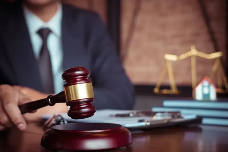 Juiz segura um martelo sobre a mesa, com a balança da justiça ao fundo