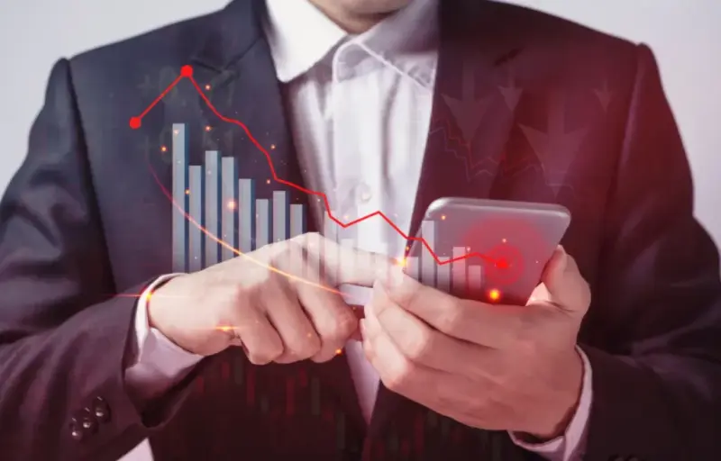 Executivo segura um smartphone, com um gráfico de queda em vermelho sobreposto à imagem