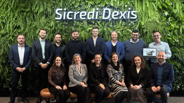 Equipe da Sicredi Dexis reunida em frente a uma parede verde com o nome da cooperativa